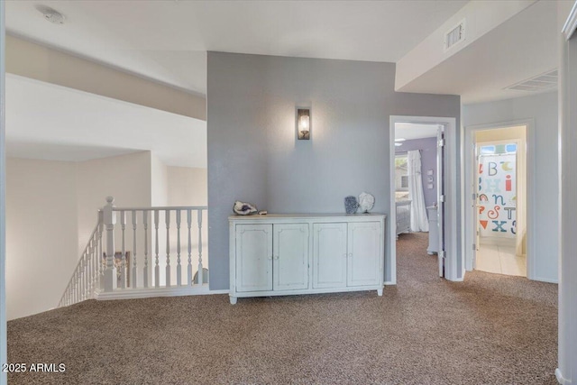 hall with carpet floors, visible vents, and an upstairs landing