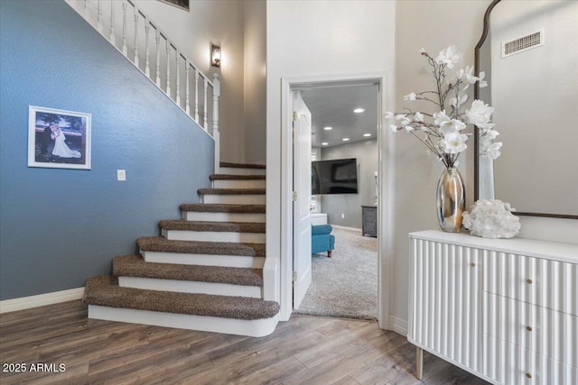 stairs featuring visible vents, baseboards, a towering ceiling, and wood finished floors