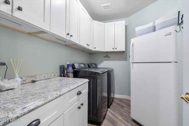 laundry area with independent washer and dryer, visible vents, cabinet space, wood finished floors, and baseboards