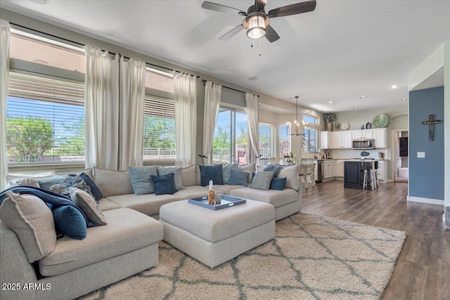 living room featuring recessed lighting, baseboards, ceiling fan with notable chandelier, and dark wood-style flooring