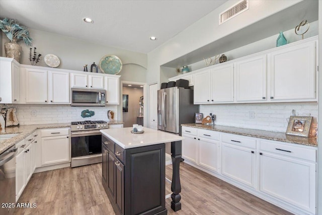 kitchen with visible vents, white cabinets, tasteful backsplash, light wood finished floors, and stainless steel appliances
