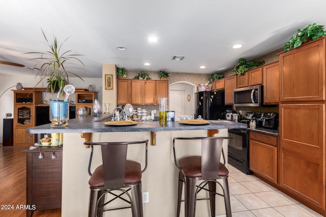 kitchen featuring an island with sink, tasteful backsplash, light hardwood / wood-style flooring, black appliances, and a breakfast bar area