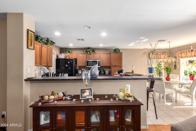 kitchen featuring light wood-type flooring, black fridge with ice dispenser, kitchen peninsula, pendant lighting, and a kitchen breakfast bar