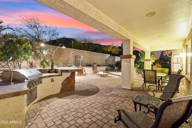 patio terrace at dusk featuring an outdoor kitchen, area for grilling, and an outdoor fire pit