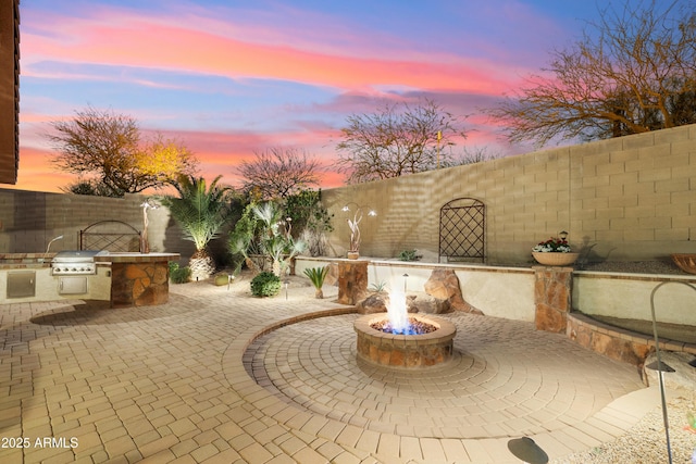 patio terrace at dusk with grilling area, exterior kitchen, and a fire pit