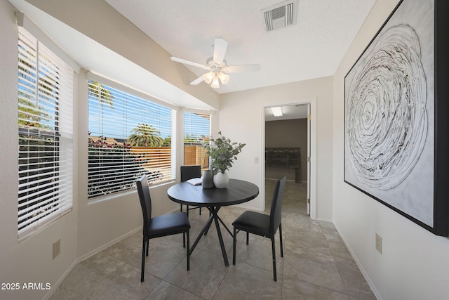 dining space featuring baseboards, visible vents, a ceiling fan, and a textured ceiling