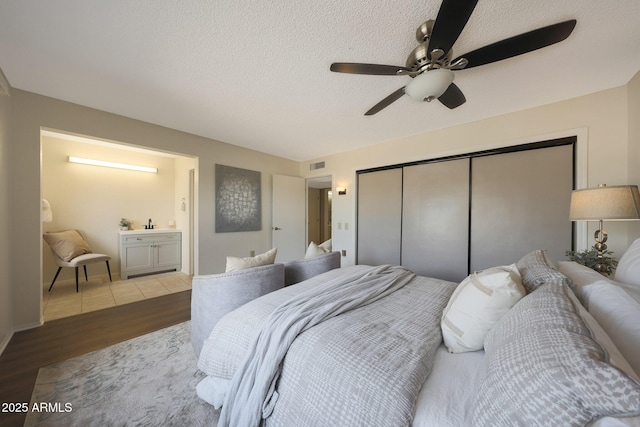 bedroom with a closet, ensuite bath, a ceiling fan, visible vents, and wood finished floors