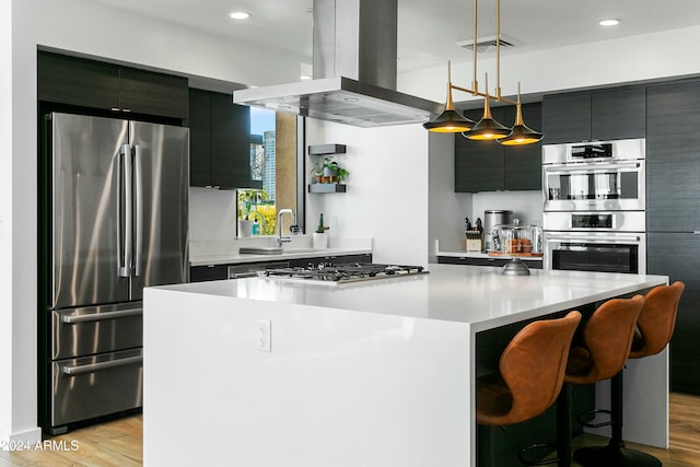 kitchen with a center island, stainless steel appliances, hanging light fixtures, island range hood, and light wood-type flooring