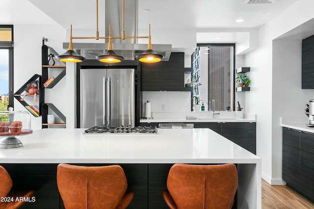 kitchen with sink, light hardwood / wood-style floors, decorative light fixtures, a kitchen bar, and appliances with stainless steel finishes