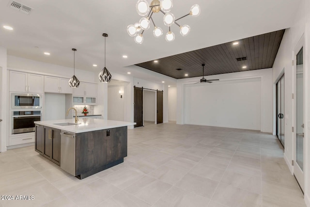 kitchen featuring appliances with stainless steel finishes, sink, an island with sink, a barn door, and white cabinets