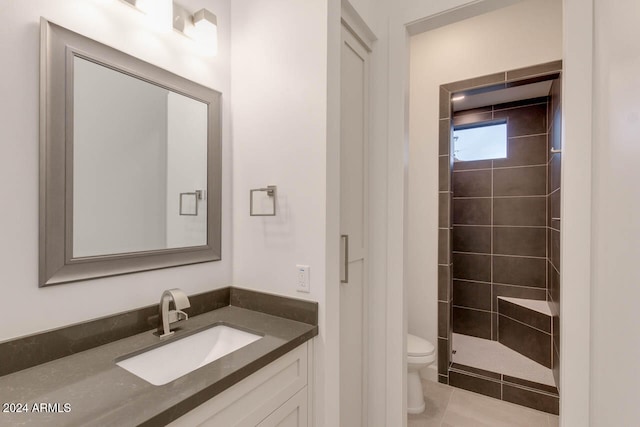 bathroom with vanity, a tile shower, toilet, and tile patterned flooring