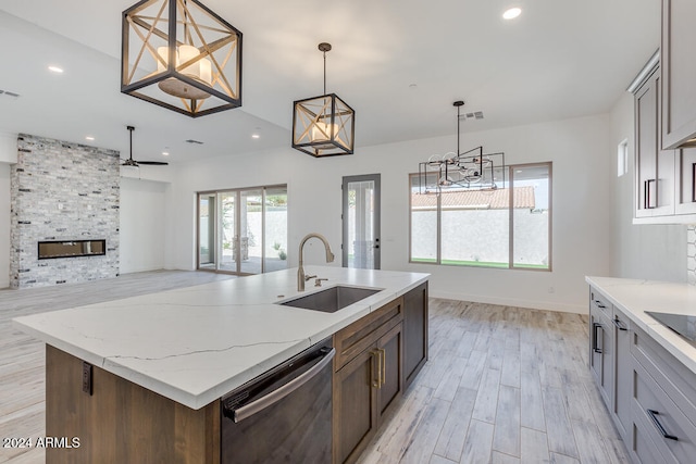 kitchen with a stone fireplace, decorative light fixtures, stainless steel dishwasher, light hardwood / wood-style flooring, and a center island with sink