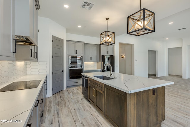 kitchen with black appliances, sink, an island with sink, pendant lighting, and light hardwood / wood-style flooring