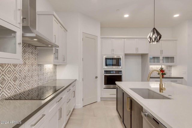 kitchen featuring appliances with stainless steel finishes, white cabinetry, decorative light fixtures, and wall chimney range hood