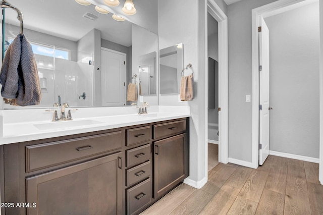 bathroom with wood finished floors, a shower stall, double vanity, and a sink