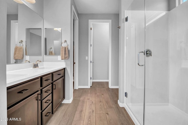 full bathroom with wood finished floors, a shower stall, vanity, and baseboards