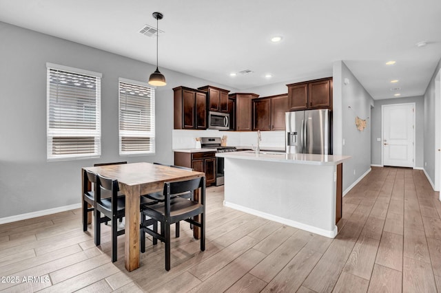 kitchen featuring light wood-style floors, stainless steel appliances, dark brown cabinets, light countertops, and baseboards