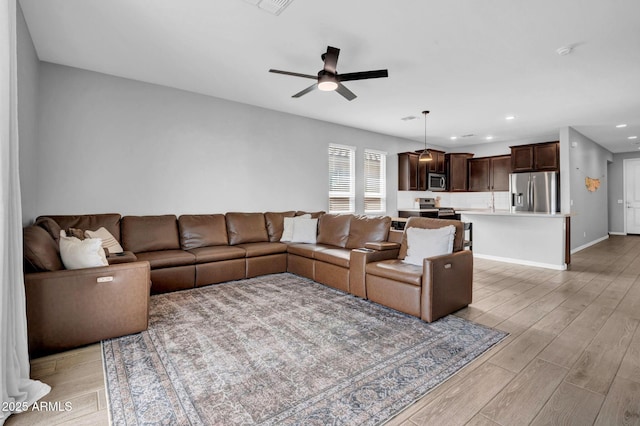 living area with recessed lighting, a ceiling fan, baseboards, and light wood-style floors