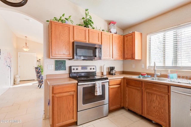 kitchen with appliances with stainless steel finishes, sink, light tile patterned floors, decorative light fixtures, and lofted ceiling