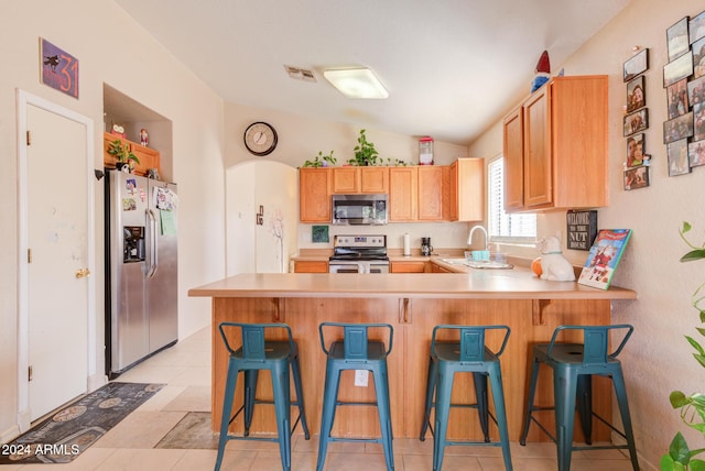 kitchen with lofted ceiling, sink, appliances with stainless steel finishes, kitchen peninsula, and a breakfast bar area