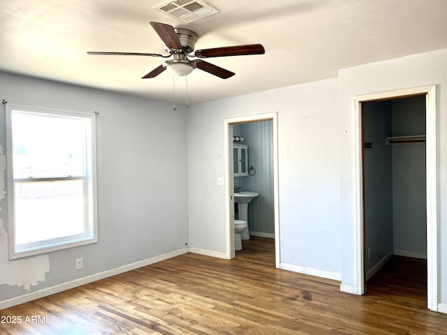 709 W Maple St, Winslow, AZ 86047 - unfurnished bedroom featuring a walk in closet, wood finished floors, a closet, baseboards, and connected bathroom
