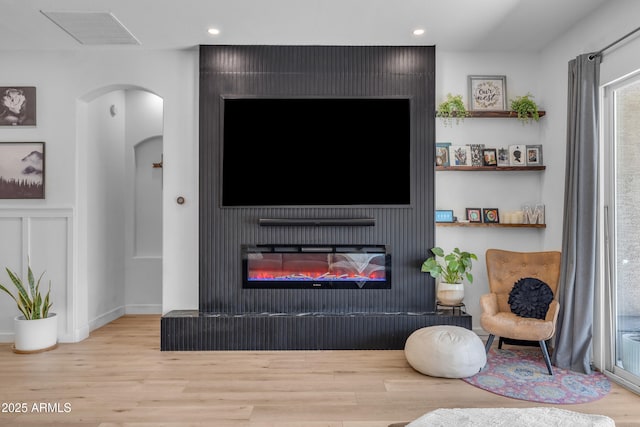 living room featuring visible vents, arched walkways, wood finished floors, a glass covered fireplace, and recessed lighting