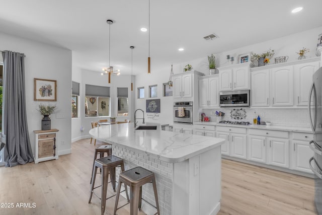 kitchen featuring visible vents, a kitchen bar, tasteful backsplash, a sink, and stainless steel appliances