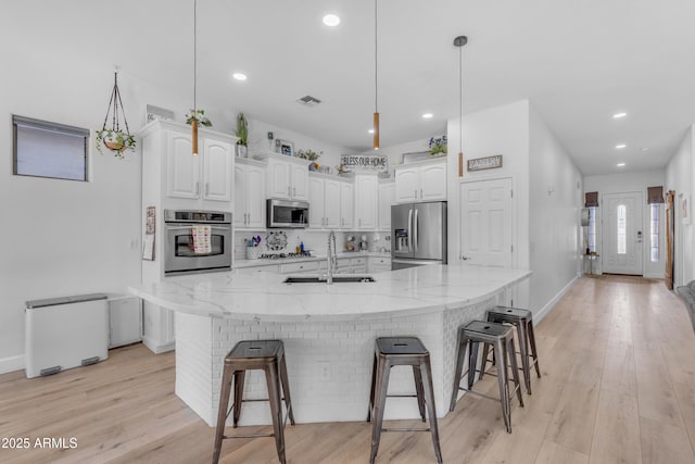 kitchen featuring white cabinets, a sink, stainless steel appliances, recessed lighting, and a kitchen bar