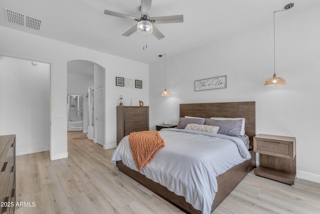 bedroom featuring visible vents, ensuite bathroom, baseboards, arched walkways, and light wood finished floors