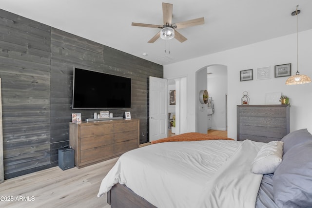 bedroom with arched walkways, light wood finished floors, a ceiling fan, and an accent wall
