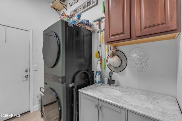 laundry room featuring cabinet space, stacked washer and dryer, and a sink