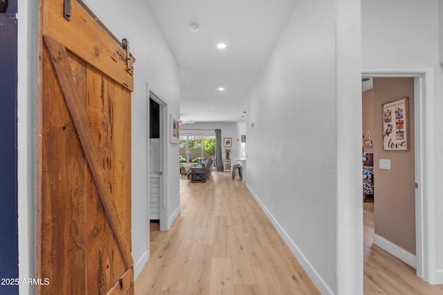 corridor with recessed lighting, baseboards, a barn door, and light wood finished floors
