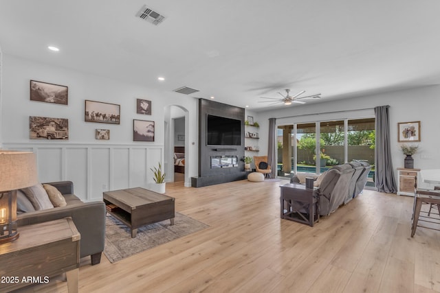 living room with arched walkways, ceiling fan, visible vents, and light wood finished floors