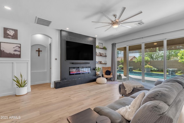 living room featuring visible vents, arched walkways, ceiling fan, and a large fireplace