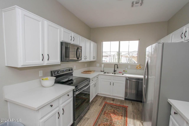 kitchen with light wood-type flooring, appliances with stainless steel finishes, sink, and white cabinetry