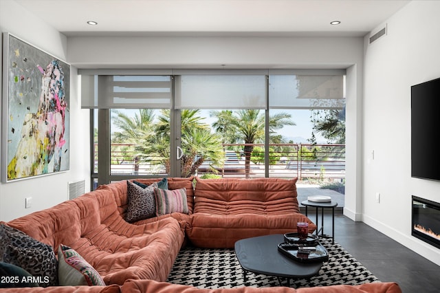 living area with finished concrete flooring, baseboards, a glass covered fireplace, and visible vents