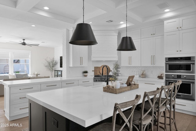 3173 E Page Ave, Gilbert, AZ 85234 - kitchen featuring tasteful backsplash, light countertops, a kitchen island with sink, light wood finished floors, and stainless steel double oven