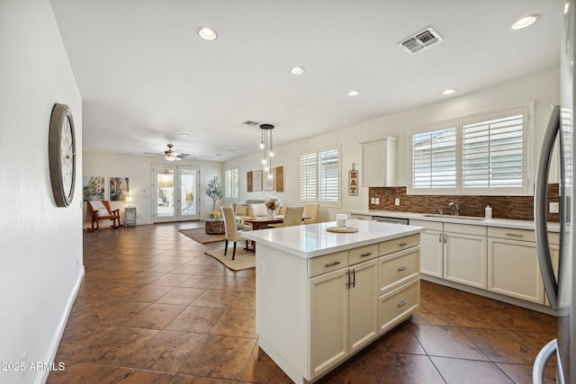 kitchen featuring light countertops, visible vents, decorative backsplash, open floor plan, and a sink