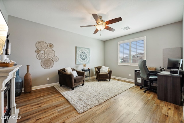 office area with a glass covered fireplace, visible vents, light wood-style flooring, and baseboards