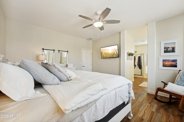 bedroom featuring a warm lit fireplace, ceiling fan, baseboards, and wood finished floors