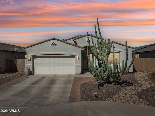 view of front facade featuring an attached garage, fence, driveway, a tiled roof, and stucco siding