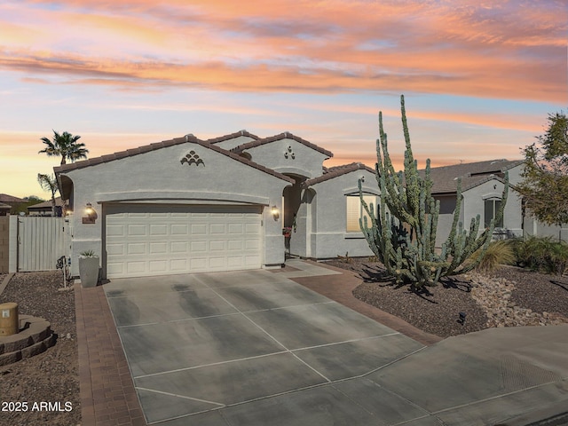 mediterranean / spanish-style home featuring a garage, driveway, a tiled roof, and stucco siding