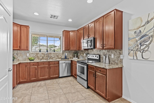 kitchen with a sink, stainless steel appliances, decorative backsplash, visible vents, and light stone counters