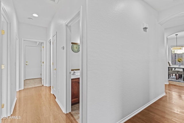 hallway with arched walkways, baseboards, and light wood-style floors