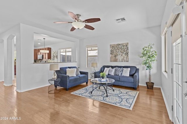 living area with arched walkways, ceiling fan, light wood finished floors, baseboards, and visible vents