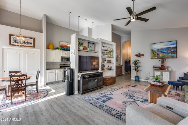 living room featuring light hardwood / wood-style floors, ceiling fan with notable chandelier, and vaulted ceiling