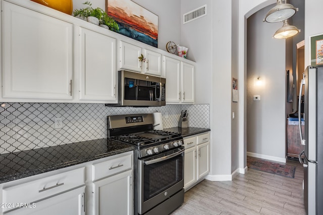 kitchen with stainless steel appliances, decorative backsplash, light hardwood / wood-style floors, white cabinets, and dark stone countertops