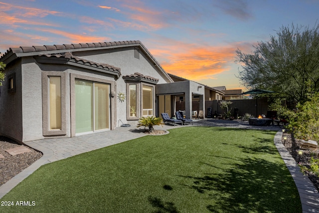 back house at dusk with a patio and a yard