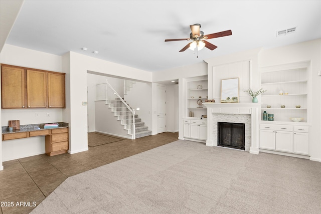 carpeted living area featuring built in shelves, a fireplace, visible vents, stairs, and built in desk