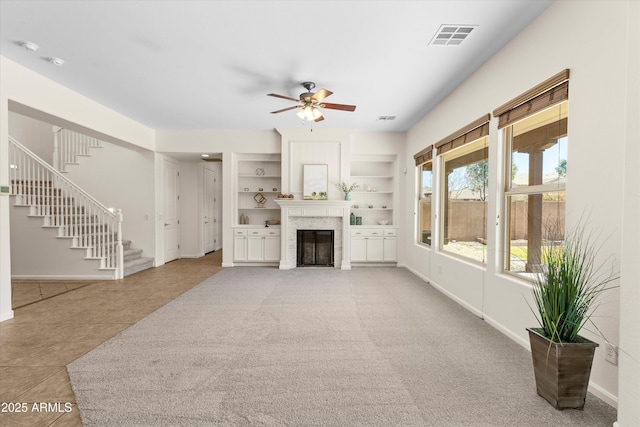 unfurnished living room with baseboards, visible vents, built in features, ceiling fan, and stairway